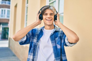 Genç İspanyol adam şehirde akıllı telefon ve kulaklık kullanarak mutlu gülümsüyor..