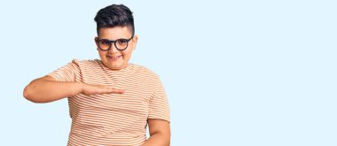 Küçük çocuk gündelik giysiler ve gözlük takıyor. Elleriyle işaret ediyor. Ölçü sembolü. Kameraya bakıp gülümsüyor. ölçüm kavramı. 