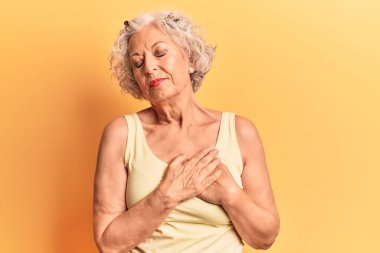 Üstün gri saçlı, günlük kıyafetler giyen, elleri göğsünde, gözleri kapalı gülümseyen ve yüzünde minnet ifadesi olan bir kadın. sağlık kavramı. 