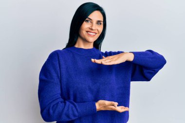 Kafkasyalı genç bir kadın, sıradan kıyafetler giyiyor. Elleriyle işaret ediyor. Ölçü sembolü. Kameraya bakıp gülümsüyor. ölçüm kavramı. 