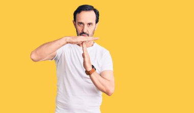 Orta yaşlı yakışıklı bir adam günlük tişört giyiyor. Elleriyle jest yapıyor, hayal kırıklığına uğramış ve ciddi bir yüz ifadesi takınıyor. 