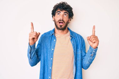 Kıvırcık saçlı ve ayı gibi giyinmiş yakışıklı genç adam şaşkın şaşkın yukarı bakıyor ve parmaklarıyla işaret ediyor ve kollarını kaldırıyor.. 