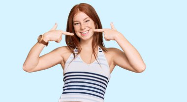 Gündelik kıyafetler giyen, neşeli gülümseyen, parmaklarıyla ve ağzıyla işaret eden genç, okumuş bir kadın. diş sağlığı kavramı. 