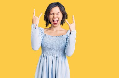 Genç ve güzel bir kız, gündelik giysiler içinde çılgın bir ifadeyle bağırıyor ve elleri havada rock sembolü yapıyor. Müzik yıldızı. ağır müzik konsepti. 