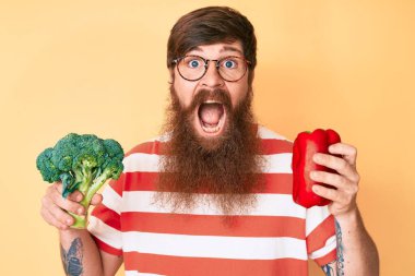 Uzun sakallı, elinde brokoli ve kırmızı biberli yakışıklı genç adam çılgınlığı kutluyor ve başarıyı hayretle haykırıyor.. 