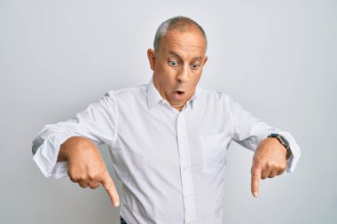 Yakışıklı, beyaz tişörtlü, reklamını gösteren parmaklarıyla aşağıya bakan, şaşırmış yüzlü ve ağzı açık bir adam. 