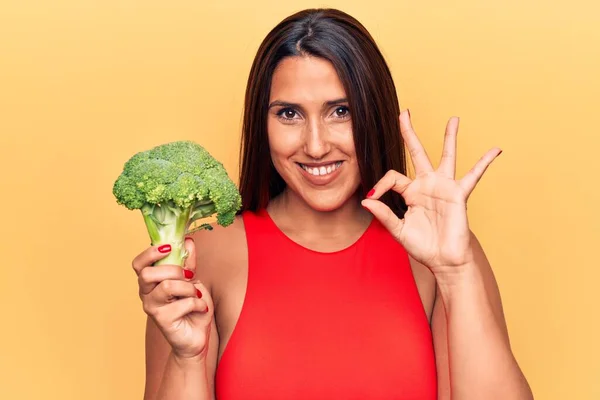 Young Beautiful Brunette Woman Holding Broccoli Doing Sign Fingers Smiling — Stock fotografie