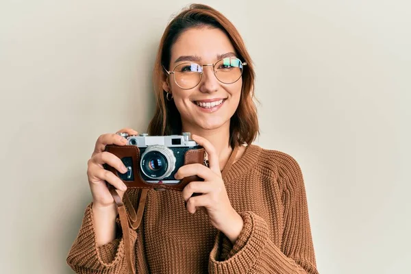 Young caucasian woman holding vintage camera smiling with a happy and cool smile on face. showing teeth.