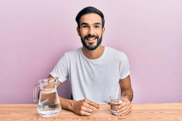 Joven Hombre Hispano Bebiendo Vaso Agua Sentado Mesa Luciendo Positivo — Foto de Stock
