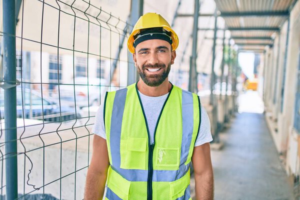 Young hispanic workman smiling happy walking at street of city