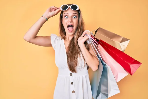 Young blonde girl holding shopping bags celebrating crazy and amazed for success with open eyes screaming excited.