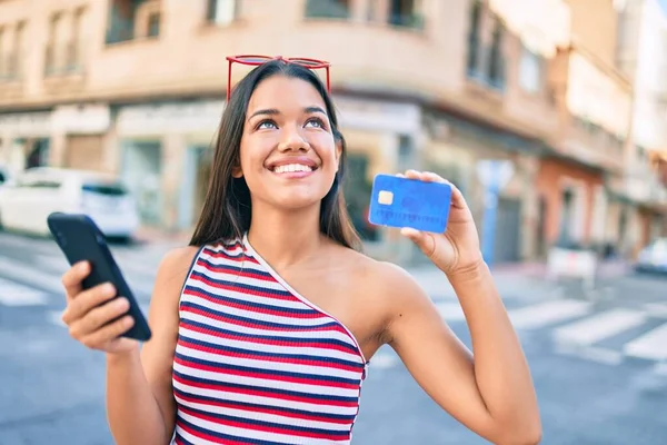 若いラテン語の女の子は スマートフォンを使用して幸せな笑顔と市内でクレジットカードを表示 — ストック写真