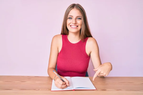 Jovem Caucasiana Escrevendo Caderno Sentado Mesa Sorrindo Feliz Apontando Com — Fotografia de Stock