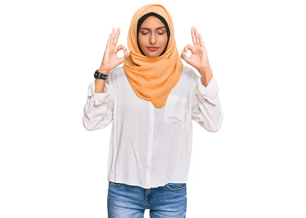 伝統的なイスラムのヒジャーブスカーフを身に着けている若いブルネットの女性は 指で瞑想のジェスチャーをして閉じ目でリラックスして笑顔 ヨガのコンセプト — ストック写真