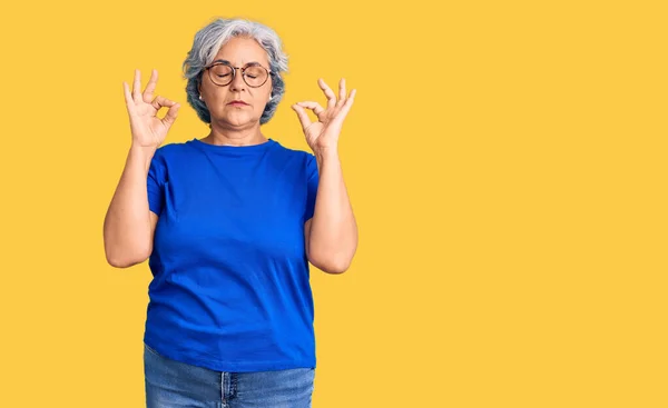 白发苍苍的老妇人穿着休闲装 戴着眼镜 闭着眼睛 微笑着 用手指做冥想动作 瑜伽概念 — 图库照片