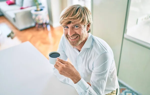 Joven Irlandés Sonriendo Feliz Bebiendo Taza Café Sentado Mesa Casa —  Fotos de Stock