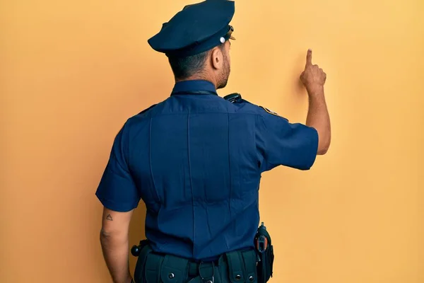 Hezký Hispánec Policejní Uniformě Pózující Pozpátku Ukazuje Prstem Dopředu — Stock fotografie