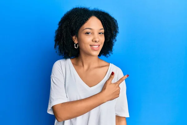 穿着休闲装的白色T恤的年轻的非洲裔美国姑娘高兴地微笑着 手指头指向旁边 — 图库照片