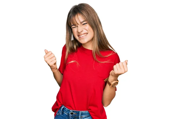年轻的高加索女孩穿着休闲的红色T恤 高兴而兴奋地举起双臂做着获胜的手势 微笑着 尖叫着要成功 庆祝概念 — 图库照片