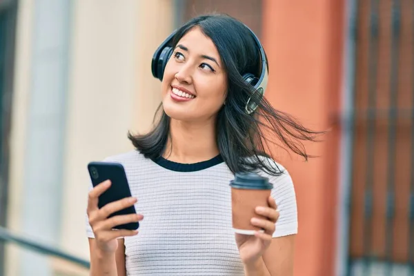 若いヒスパニック女性はコーヒーを飲み 市内でスマートフォンやヘッドフォンを使用しています — ストック写真