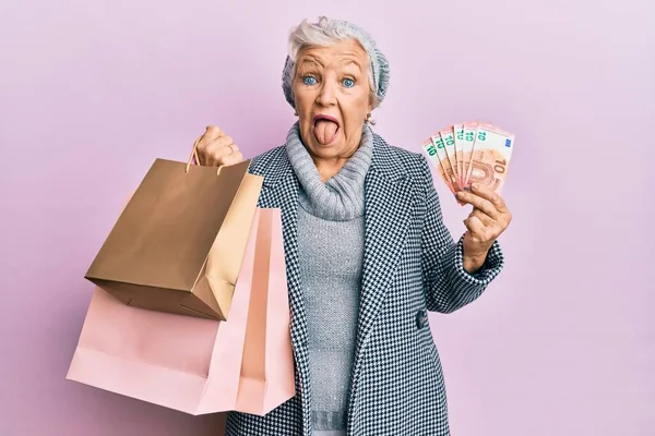 Senior Gråhårig Kvinna Som Håller Shoppingväskor Och Eurosedlar Sticker Tunga — Stockfoto