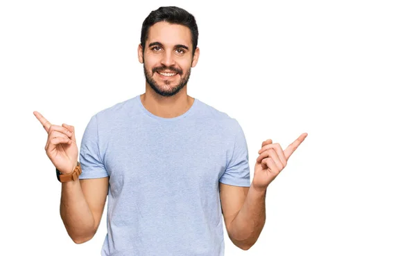 若いヒスパニック系の男性が別の方向に指で自信を持って指して笑顔カジュアルな服を着て 広告のコピースペース — ストック写真