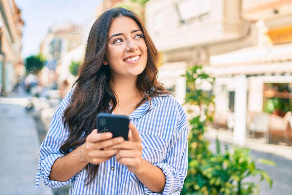 Young hispanic businesswoman smiling happy using smartphone at the city.