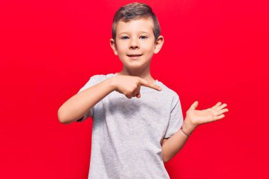 Hoş sarışın çocuk gündelik giysiler giyip kameraya hayret ediyor ve gülümsüyor.. 