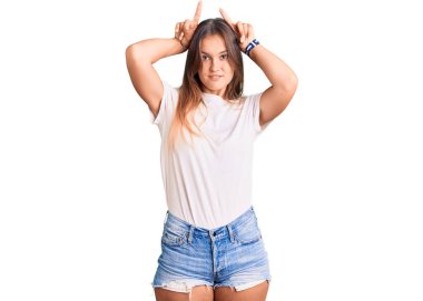 Güzel beyaz tişört giyen beyaz kadın boynuzları gibi parmağıyla komik jestler yapıyor. 