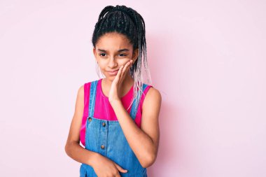 Saçları pembe arka plan üzerine günlük kıyafetler giyen, diş ağrısı ya da diş ağrısı yüzünden ağızlarına acı dolu bir ifadeyle dokunan Afrikalı Amerikalı genç bir kız. dişçi 