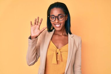 Genç afro-amerikan kadın iş kıyafetleri giyer ve parmaklarıyla 5 numarayı gösterirken kendinden emin ve mutlu gülümserken.. 