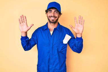 Kıvırcık saçlı ve ayı gibi giyinmiş yakışıklı genç adam on numarayı gösterip, parmaklarını gösterirken kendinden emin ve mutlu gülümsüyor.. 