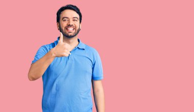 Gündelik kıyafetler giyen genç İspanyol adam elleriyle mutlu bir jest yapıyor. Kameraya bakıp başarıyı gösteren ifade. 