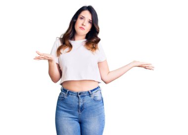 Güzel, genç, esmer, sıradan kıyafetler giyen, kafası karışmış, elleri ve kolları havada bir kadın. şüphe kavramı. 