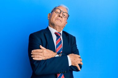 İş elbisesi ve kravat takmış, kolları çapraz ve kendinden emin bir şekilde yana bakan kıdemli beyaz adam. 