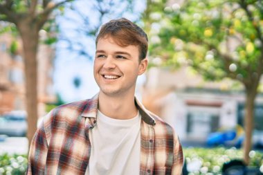 Genç beyaz adam gülümseyerek şehirde mutlu mesut duruyor..