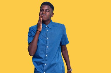 Sıradan kıyafetler giyen, diş ağrısı ya da diş hastalığından dolayı acı dolu bir ifadeyle dudaklarına dokunan Afrikalı genç bir Amerikalı. dişçi 