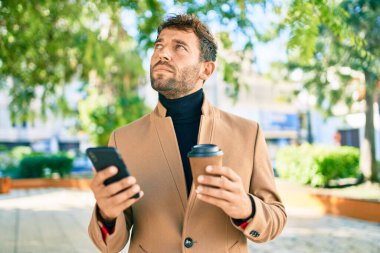 Zarif ceketli yakışıklı bir iş adamı. Açık havada akıllı telefon kullanıyor.