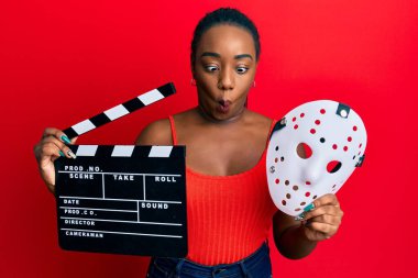 Genç Afro-Amerikalı kadın elinde video film panosu ve korku maskesi ile balık suratlı ve şaşı gözlü çılgın ve komik.. 