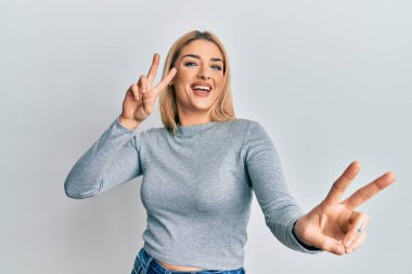 Gündelik giysiler giymiş genç beyaz kadın kameraya bakıp zafer işareti yapıyor. İki numara.. 