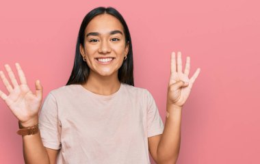 Genç Asyalı kadın gündelik giysiler giyer ve dokuz numaralı parmaklarıyla gülümseyerek mutlu ve kendinden emin bir şekilde işaret eder.. 