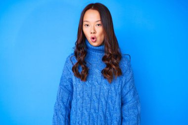 Young beautiful chinese girl wearing casual winter sweater afraid and shocked with surprise expression, fear and excited face. 