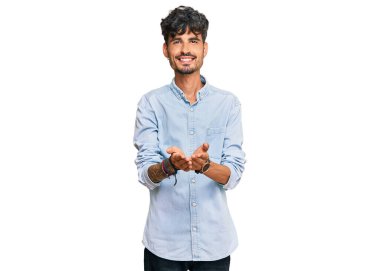 Elleri avuçlarında gülümseyen ya da el hareketi yapan gündelik kıyafetler giyen İspanyol genç bir adam. Bekleme ve koruma 