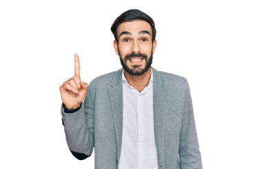 Genç İspanyol adam iş kıyafetleri giyip bir numarayı gösterip işaret ederken kendinden emin ve mutlu bir şekilde gülümsüyor.. 