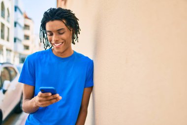 Genç Afrikalı Amerikalı mutlu gülümsüyor. Duvara dayanmış akıllı telefon kullanıyor..