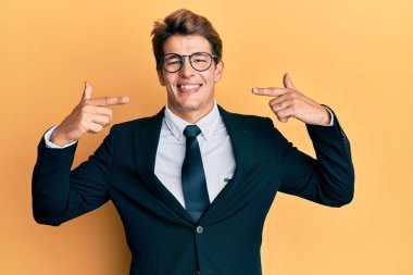 İş elbisesi giyen, kravatlı, neşeli gülümseyen, parmaklarıyla ve ağzıyla işaret eden yakışıklı beyaz bir adam. diş sağlığı kavramı. 