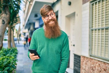 Kızıl saçlı, mutlu gülümseyen ve şehirde akıllı telefon kullanan genç bir İrlandalı..