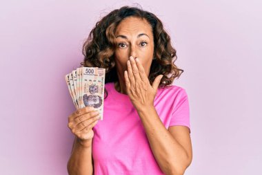 Orta yaşlı İspanyol kadın, Meksika pesolarını elinde tutuyor. Ağzını eliyle kapatıyor. Şok olmuş ve hata yapmaktan korkuyor. şaşırmış ifade 