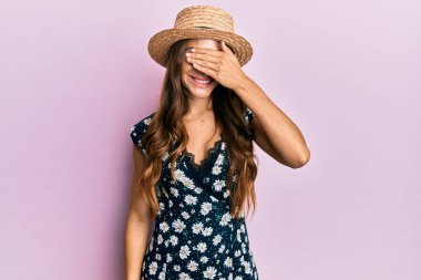 Genç esmer kadın, yaz şapkası takıyor, gülümsüyor ve elleri yüzünde, şaşırtmak için gözleri örtüyor. kör kavram. 