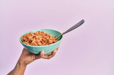 İtalyan eriştesiyle izole edilmiş pembe arka planda duran İspanyol adamın eli..